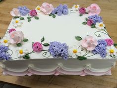 a white cake with pink, purple and yellow flowers on it sitting on a wooden table