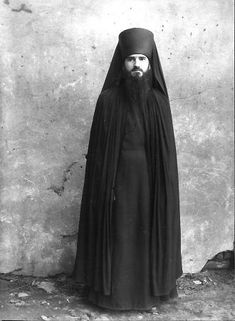 an old photo of a man with a long beard wearing a black robe and standing in front of a wall