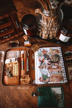 a wooden table topped with an open notebook and lots of things on top of it