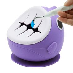 a hand is holding a toothbrush in front of a purple toy with teeth on it