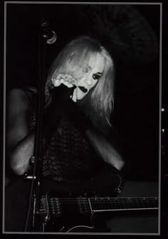 a black and white photo of a woman singing into a microphone while playing an electric guitar