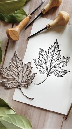 some leaves are sitting on top of a piece of paper next to paintbrushes