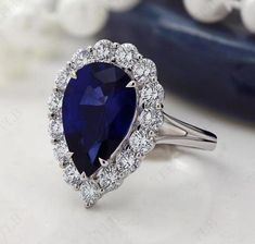 a pear shaped blue sapphire and diamond ring on a white surface with other jewelry items in the background