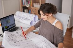 a woman sitting at a desk working on blueprints