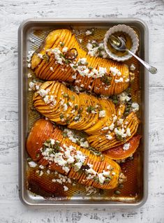 baked sweet potatoes with feta cheese and herbs in a baking pan on a white wooden table