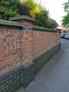 a red brick wall next to a street with cars parked on the side and trees in the background