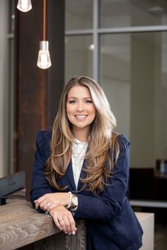 a woman standing in front of a wooden table with her arms crossed and looking at the camera