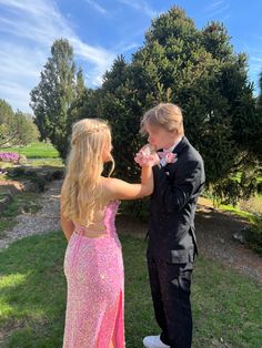 a young man and woman in formal wear eating cake together outside on the grass with trees behind them