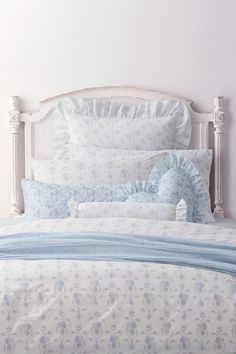 a white bed with blue and white comforter on it's headboard in a bedroom