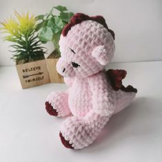 a pink crocheted stuffed animal sitting next to a potted plant on a table