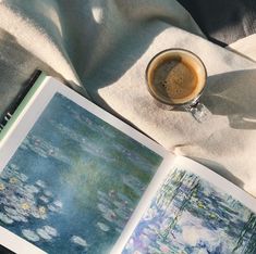 an open book sitting on top of a table next to a cup of coffee and water lilies