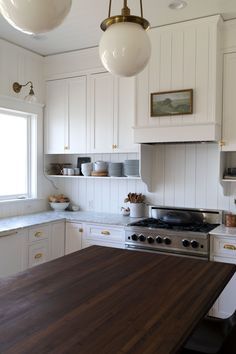 a kitchen with white cabinets and wood counter tops, two pendant lights over the stove