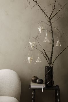 a vase with some branches in it next to a white chair and a book on a table