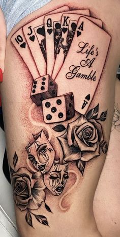 a woman's thigh with playing cards and roses on it, as well as two dice