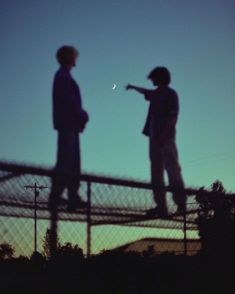 two people standing on top of a fence with the moon in the sky behind them