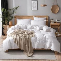 a bed with white linens and pillows in a neutral bedroom, next to a potted plant