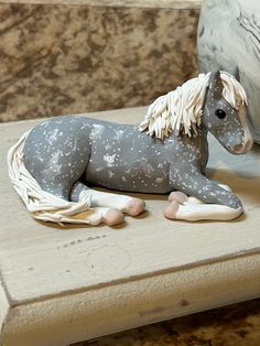 a gray and white horse figurine sitting on top of a wooden table next to a pillow