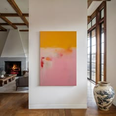 an abstract painting hangs on the wall next to a large vase in front of a fireplace