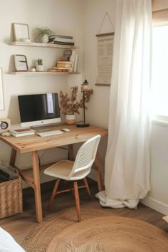 a desk with a computer on top of it next to a white chair and window