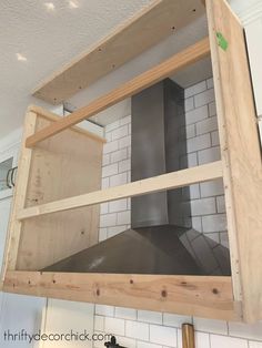 a kitchen with white tile and wooden shelves above the stove top, in front of a wall mounted range hood