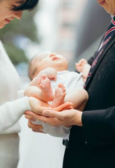 a woman holding a baby in her hands while standing next to an adult and child