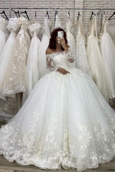 a woman taking a selfie in front of wedding gowns on display at a store