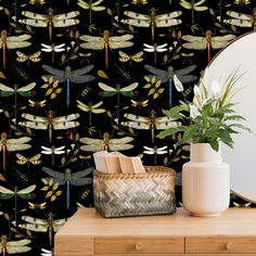 a mirror and vase on a dresser in front of a wallpaper with dragonflies