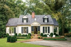 a small white house with black shutters and green trees in the front yard area