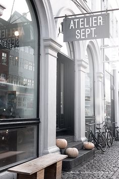 an empty bench in front of a storefront on a cobblestone street with bicycles parked outside