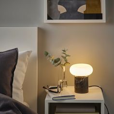 a bedside table with a lamp, book and plant on it next to a bed