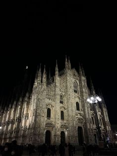 the cathedral is lit up at night with people walking in front and onlookers