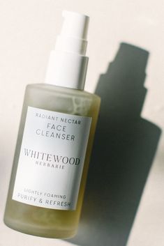 a bottle of white wood facial cleanser sitting on a table next to a shadow