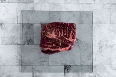 a piece of raw meat on a marble counter top with white and gray tiles in the background