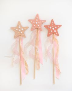 three star shaped cake toppers on sticks with pink and white ribbons around the edges