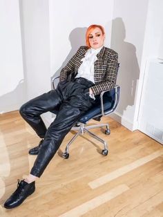 a woman with red hair sitting in a chair wearing black leather pants and a blazer