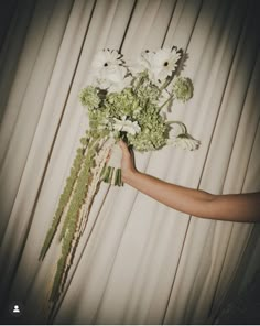 a woman holding a bouquet of flowers in front of a white curtained wall with sheer drapes