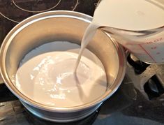 milk being poured into a metal bowl on top of a stove burner with a measuring cup next to it