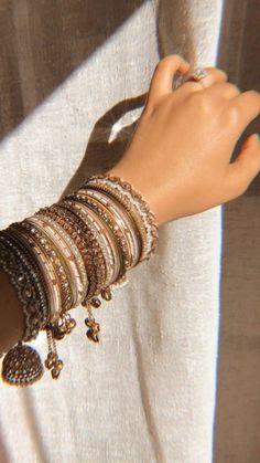 a woman's arm with bracelets and rings on it, next to a curtain