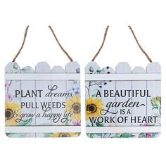 two wooden signs with flowers on them hanging from twine strings, one saying plant dreams and the other saying a beautiful garden is a work of heart