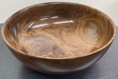 a large wooden bowl sitting on top of a black counter next to a white wall