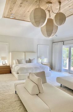 a large bedroom with white furniture and wood ceilinging, along with two lamps hanging from the ceiling