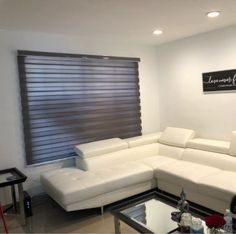 a living room with white couches and a black table in front of the window