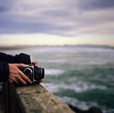 a person is holding a camera on a pier near the ocean with waves coming in