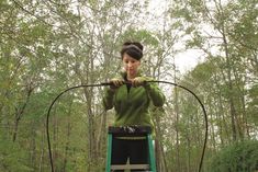 a woman standing on top of a green ladder in the middle of a wooded area