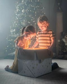 two young children opening a box with a lit candle in front of a christmas tree