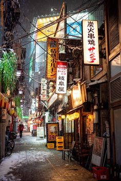 an alley way with signs and lights in the city at night time, on a snowy day