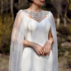 a woman wearing a white wedding gown with a veil on her head and an embellished cape over her shoulders