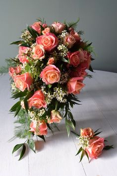 a bouquet of pink roses and greenery on a white table with two smaller ones