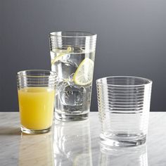 three glasses filled with orange juice on top of a white marble table next to each other