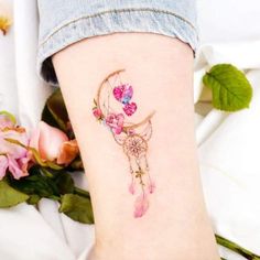 a woman's thigh with pink flowers and a dream catcher tattoo on her leg